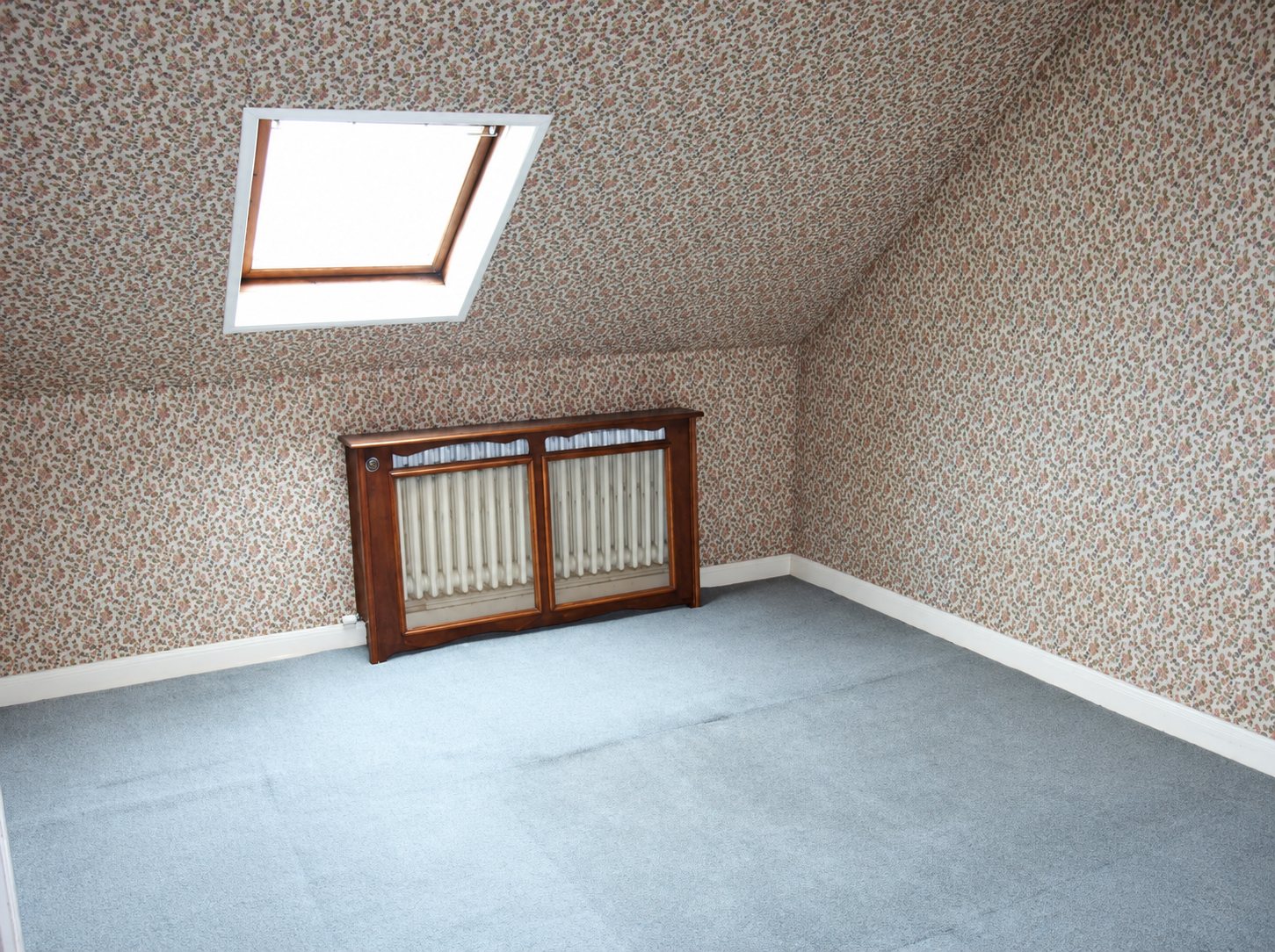 Pièce sous les combles vide, avec fenêtre de toit, papier peint fleuri et moquette bleu-gris