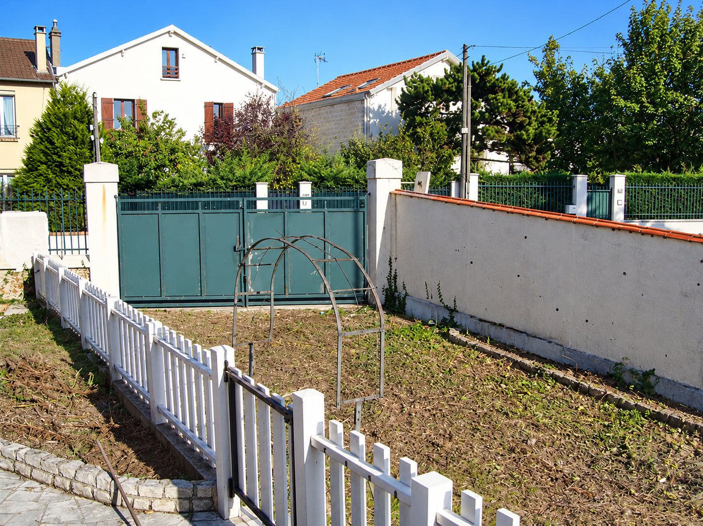 Clôture blanche et portail vert devant le mur d’un jardin