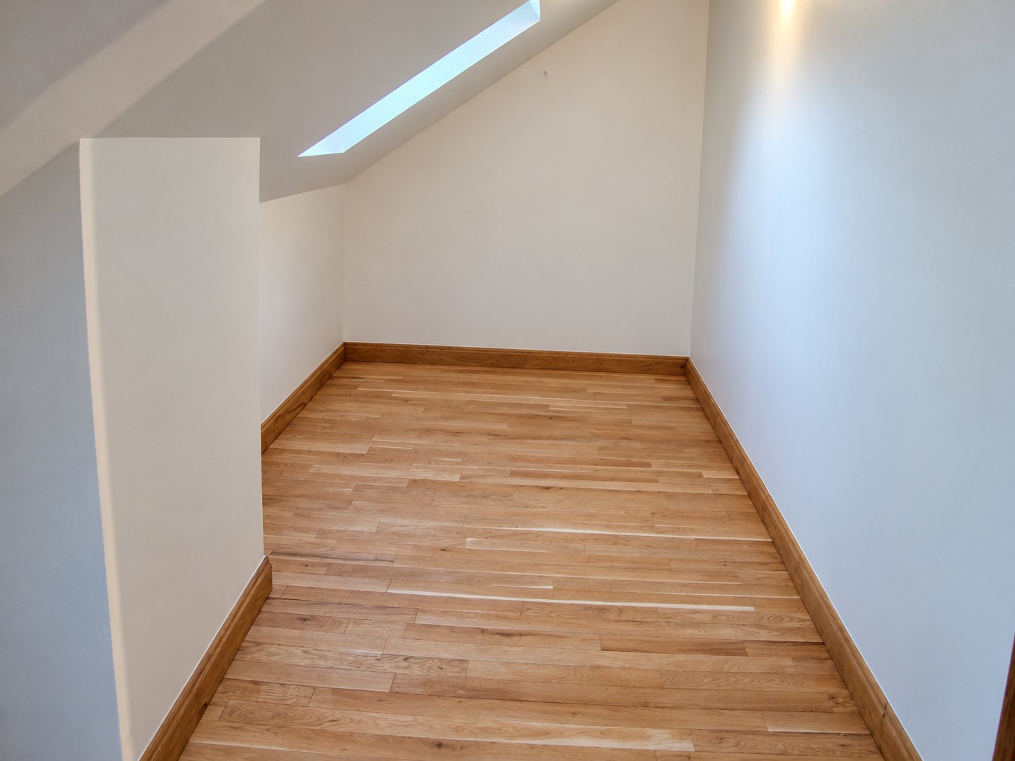 Combles aménagés avec parquet en bois clair et fenêtre de toit