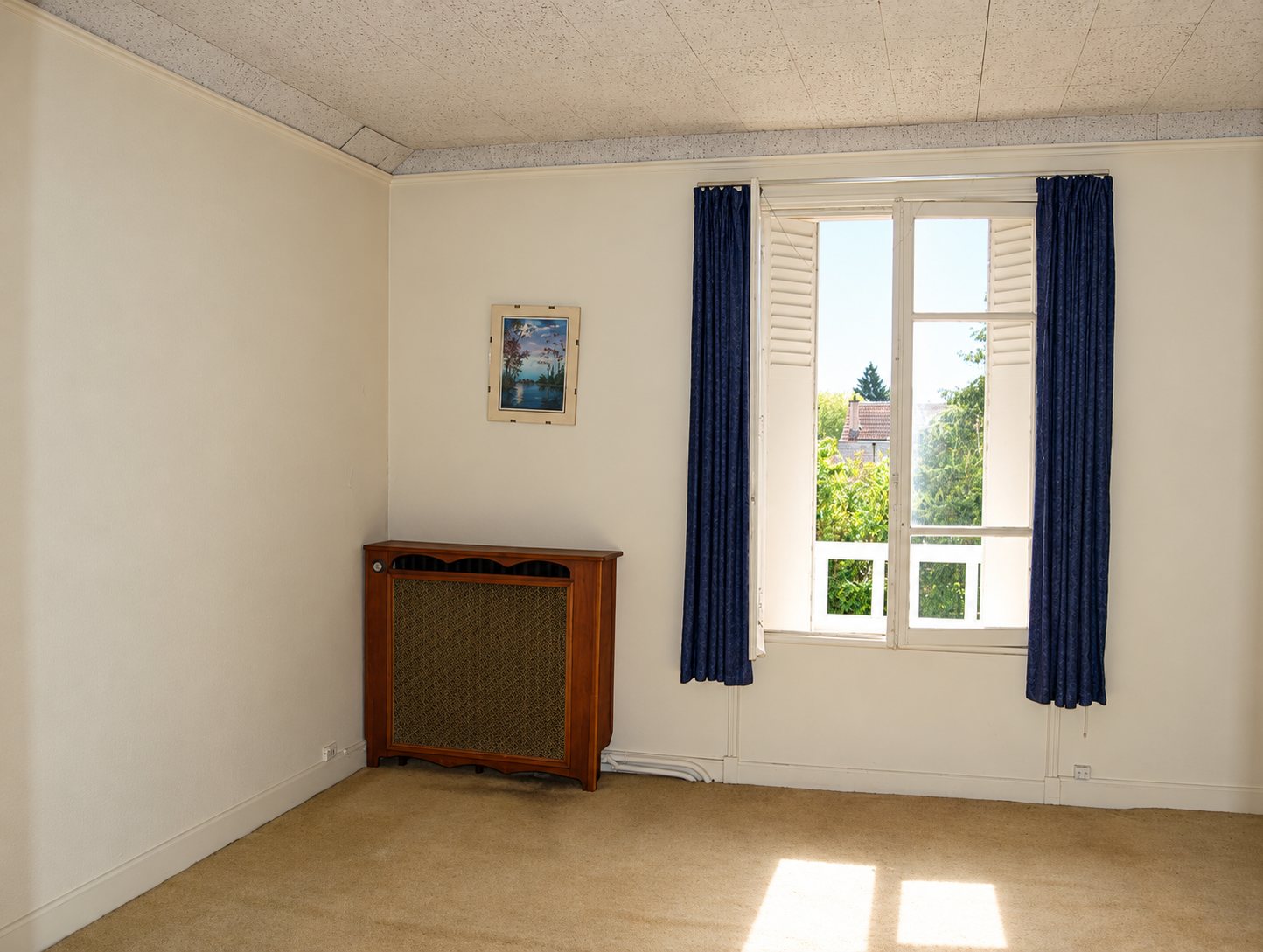 Pièce vide avec fenêtre, rideaux bleus et radiateur, avant rénovation